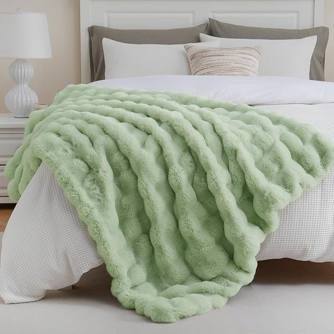 Light green blanket draped over a bed with white bedding and gray pillows.